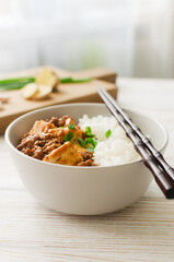 Mapo tofu dish in spicy sauce with minced beef in a ceramic bowl on a white background. Dish from Sichuan province. Traditional Asian food concept. Selective focus. Vertical orientation.