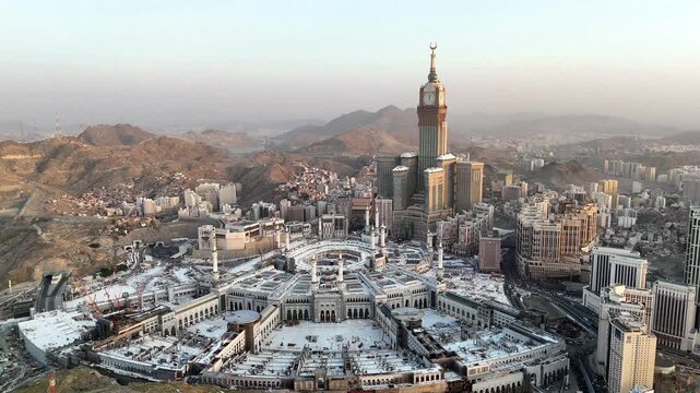 drone footage of Mecca, Saudi Arabia, filmed at sunset. The video captures the vast urban landscape with residential buildings, modern towers, and surrounding mountains bathed in golden hour light