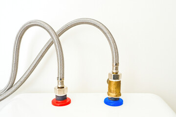 Close-up of flexible braided metal water hoses connected to hot and cold water supply with red and blue markings, plumbing installation detail.