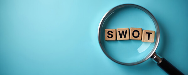 SWOT analysis letters on wooden blocks viewed through magnifying glass against blue background. Business strategy tool identifies strengths, weaknesses, opportunities, threats for corporate planning,