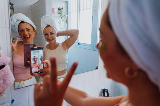 Two happy women taking selfie with under eye patches and towels on their heads - Powered by Adobe