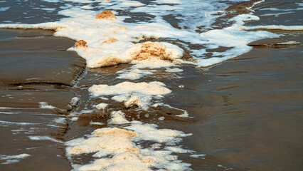 Rapid ebb, falling tide in flakes of foam from washed away organic matter on supralittoral sand coast of the South China Sea. Drain from a littoral bath. Borneo Island