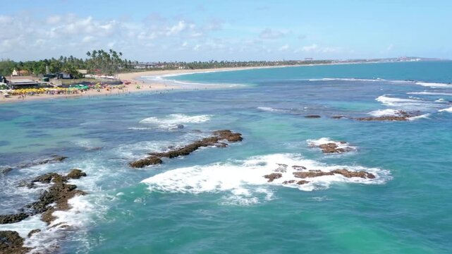 Waves crash against the rocky shore of a tropical beach on a sunny day