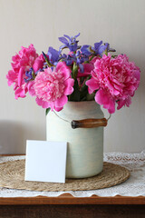 Peonies and irises bouquet in milk can with blank card