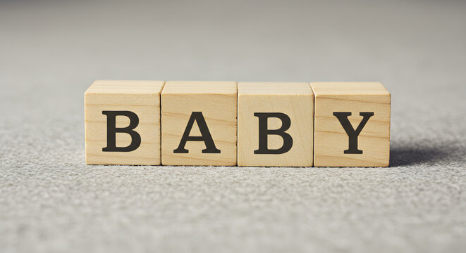 Wooden alphabet blocks spelling out the word BABY on a textured gray surface.