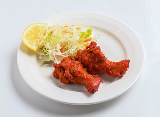 Spicy Tandoori Chicken Wings with Lemon and Salad on a White Plate isolated on white background side view of indian and pakistani food