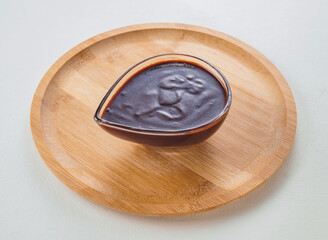 Hoisin Sauce in Glass Gravy Boat on Wood Plate isolated on white background side view of Asian dip