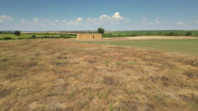 Aerial drone shot of a large stack of rectangular hay bales arranged in a geometric pattern on a harvested agricultural field, symbolizing traditional farming, rural lifestyle, and food production ind
