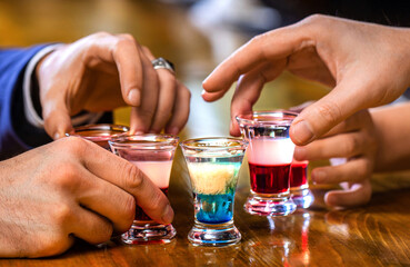 People drinking at aperitif. Several alcohol shot glasses.Shots on a bar counter top. Set of shot cocktails. Male hands cheer with glasses of vodka and liqueur