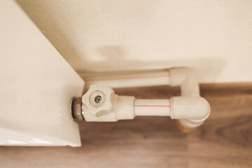 
Close up of radiator valve and heating pipe connection on wooden floor. Part of modern home heating system providing regulation and comfort in residential interior.