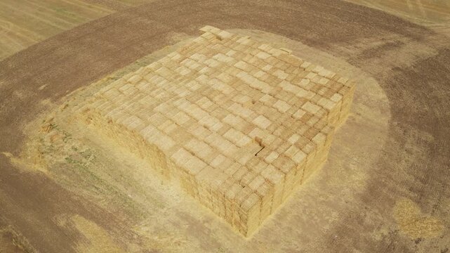 Aerial drone shot of a large stack of rectangular hay bales arranged in a geometric pattern on a harvested agricultural field, symbolizing traditional farming, rural lifestyle, and food production ind