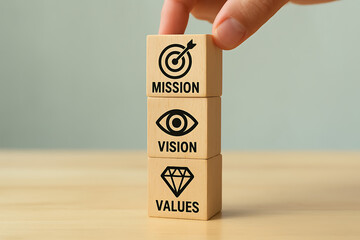 Hand stacking three wooden cubes labeled mission, vision, and values, representing the core purpose, future aspirations, and guiding principles of an organization or business