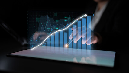 Close-up of a business professional engaging with a holographic graph display on a tablet, illustrating data trends and fostering strategic insights in a modern office. Impute