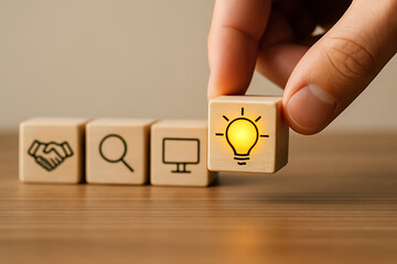 hand placing a wooden cube with a glowing light bulb icon next to a row of blocks representing business collaboration search and technology