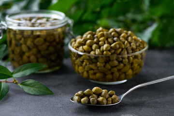 tasty pickled caper buds in a clear glass bowl on a black marble background, selective focus.Caper berry in a bowl .