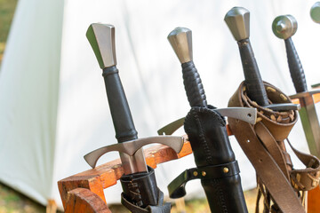 Medieval swords displayed on wooden rack at reenactment event