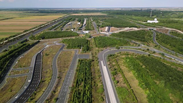 Aerial drone view of automotive test track and proving ground with multiple asphalt lanes, curves, and straights surrounded by rural farmland and green landscape for vehicle testing
