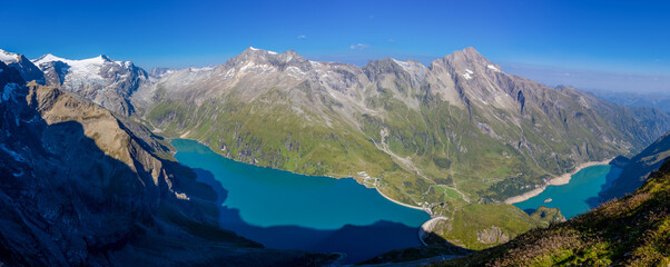 Panorama of Alps mountains on a sunny day. High resolution widescreen panorama of mountain landscape. Blue sky with some clouds above beautiful summits alpine range Stausee Mooserboden Kaprun lake and