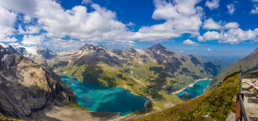 Panorama of Alps mountains on a sunny day. High resolution widescreen panorama of mountain landscape. Blue sky with some clouds above beautiful summits alpine range Stausee Mooserboden Kaprun lake and