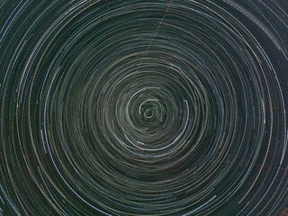 Long exposure photo of the night sky with thousands of star trails forming circles and ovals, creating abstract cosmic light patterns