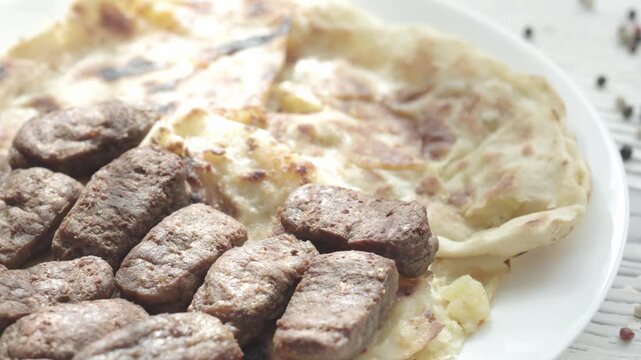 Close-Up of Romanian Mici Sausages Served with Flatbread and Tomatoes on a White Plate	