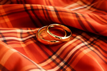 Close-up of two shiny gold wedding rings on soft orange checkered fabric symbolizing autumn - the season of weddings and marriages. Symbol of eternal love and union, copy space