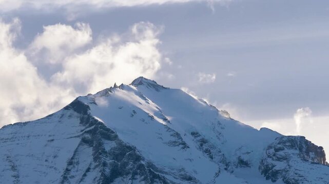Snowcapped mountain peak rises against a cloudy sky
