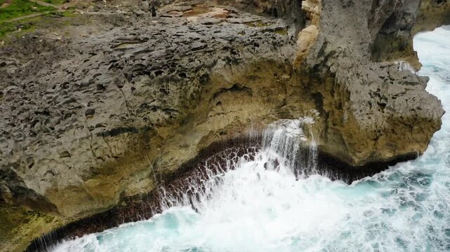 Waves crash against the rocky cliffs of nusa ceningan in indonesia