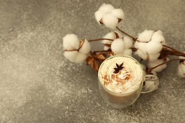 Warm seasonal drink topped with cream star anise and sprinkled spice beside cotton branches
