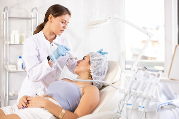 European female aesthetician making facial beauty procedure with macro molecule atomizing pen to young girl.