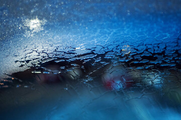 Car front glass covered with frosted ice and defrosted path with blue sunrise sky and warm city lights. Cold winter scene. Driving in dangerous conditions concept.