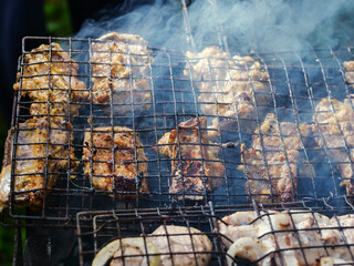 A grill full of meat is cooking over a fire. The meat is being cooked on a metal grate, and the...
