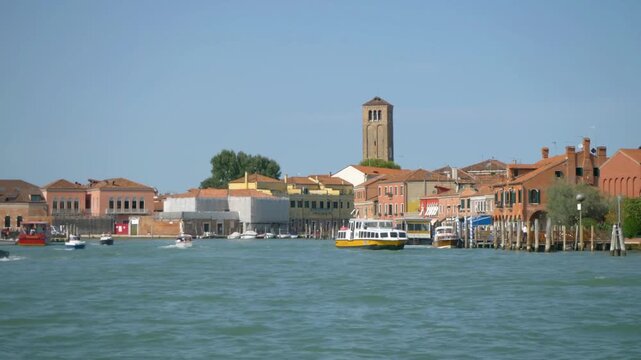 Boats sail along the waterfront of murano, italy on a sunny day