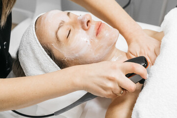 Caucasian woman receiving RF lifting treatment for facial rejuvenation, relaxing on treatment...