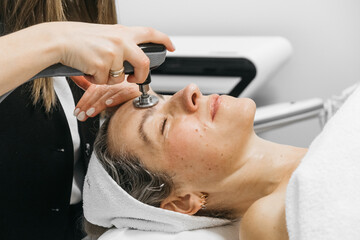 Caucasian woman receiving RF lifting treatment for facial rejuvenation, relaxing on treatment...