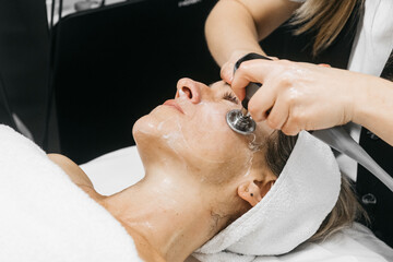 Woman receiving RF lifting treatment for facial rejuvenation, with a professional applying a device to enhance skin texture and promote youthful appearance in a serene spa environment