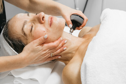 Woman receiving RF lifting treatment for facial rejuvenation, with a professional applying a device to enhance skin texture and promote youthful appearance in a serene spa environment