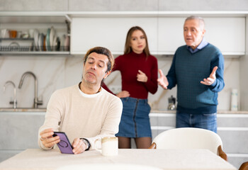 Fototapeta premium Elderly man and young woman quarreling with adult man in kitchen at home