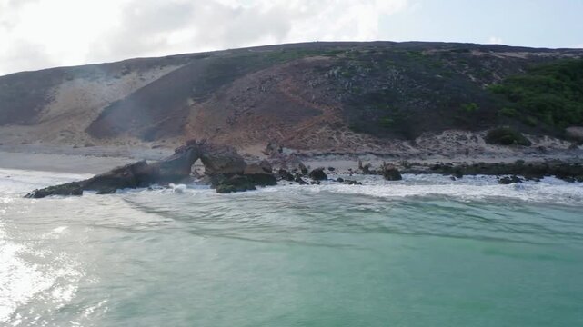 Waves gently lap against the rocky shore of a tropical island