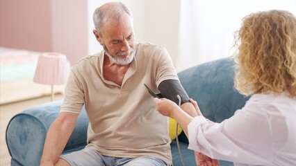 Female doctor measuring blood pressure of senior man at home