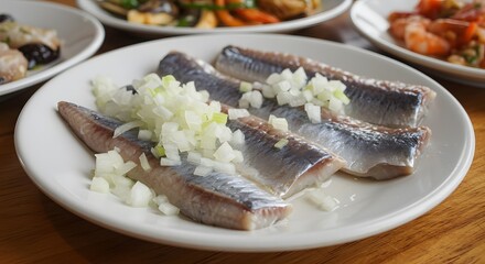 Close up of herring fillets topped with chopped onions on a white plate alongside other dishes
