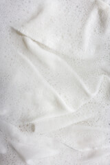 White fabric with soap foam and bubbles texture closeup, washing and cleaning background