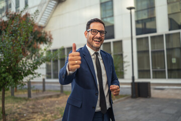 Fototapeta premium Happy businessman giving thumbs up sign smiling outdoors