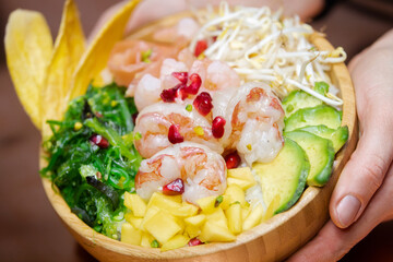 Exotic poke bowl with salmon, shrimp, avocado and mango in wooden bowl