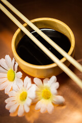 Soy sauce bowl with chopsticks and daisies on copper background