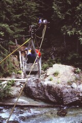 Naklejka premium People riding vintage cable car over a rushing river, crossing forest in remote wilderness, adventure travel