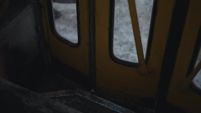 Low view of bus door opening and closing during motion, steps and yellow frame near snowy street outside, worn metal and rubber tread visible, cold winter commute mood from interior as vehicle rolls