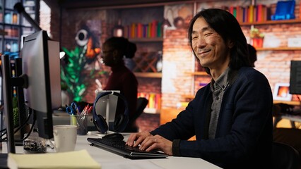 Portrait of smiling senior engineer coding advanced AI algorithm in startup office, refining...