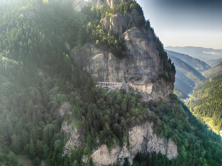 Drone shot of Sumela Monastery nestled in a steep cliffside surrounded by dense forest and mountain scenery in Trabzon, Turkey. A breathtaking view of nature and ancient architecture.