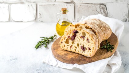 Sliced olive bread on a wooden board with oil and rosemary against a white wall